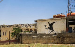 An image by Banksy of a masked man throwing a bouquet of flowers painted onto a building in Palestine.