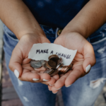 Woman holds hands out with change and a sign that reads “Make Change.”