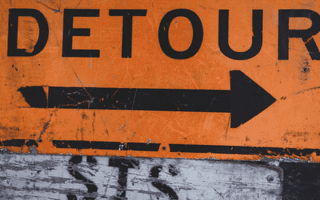 An orange and black sign with the word “DETOUR” and a black arrow pointing to the right.