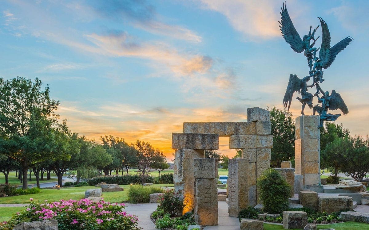 A statue on the Abilene Christian University campus with trees in the background and a sunset sky.