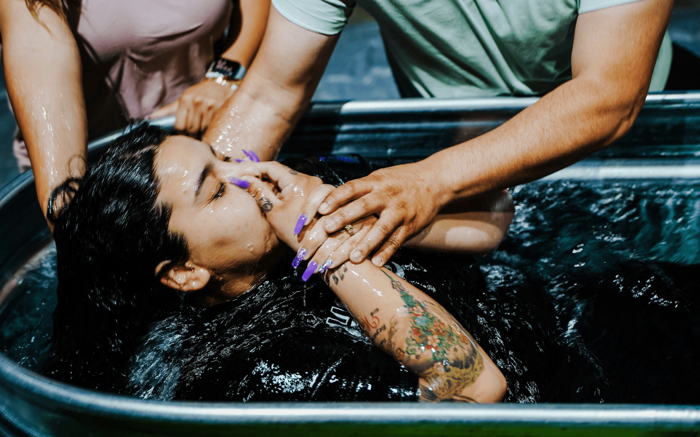 A photo of two people baptizing a young woman in a trough.
