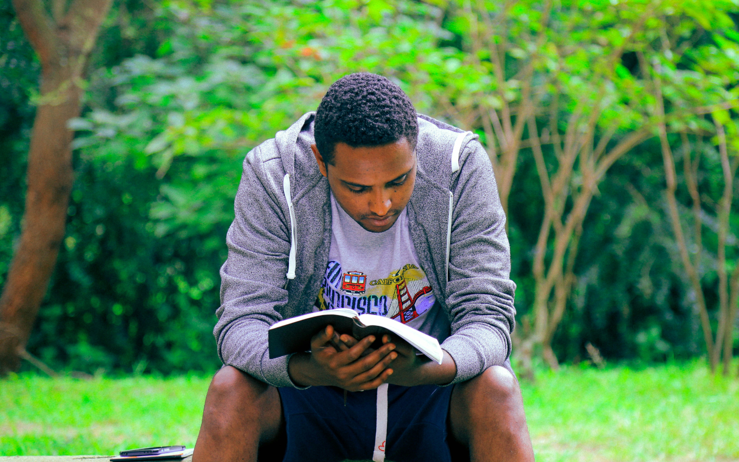 A man sitting on a park bench reading the Bible.