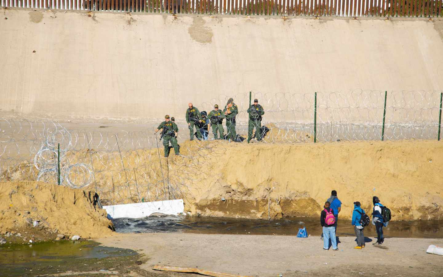 A photo of the border with immigrants facing patrol agents and razor wire.