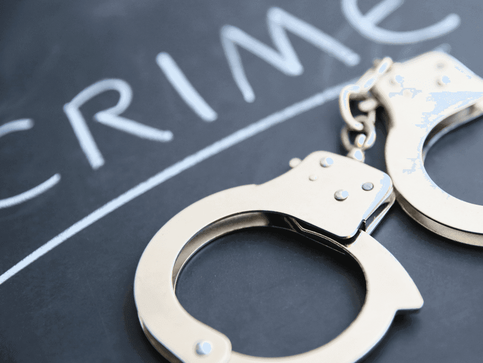 A photo of handcuffs lying on a chalkboard with the word “crime” written on it.