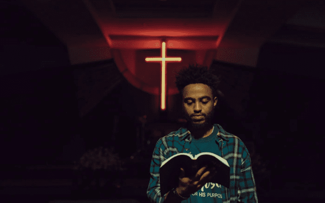 A man holding a book in front of a neon cross.