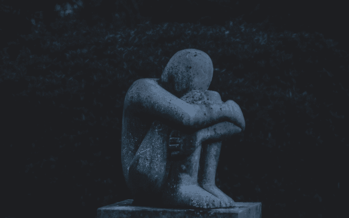 A stone sculpture of a person hugging his knees in grief.