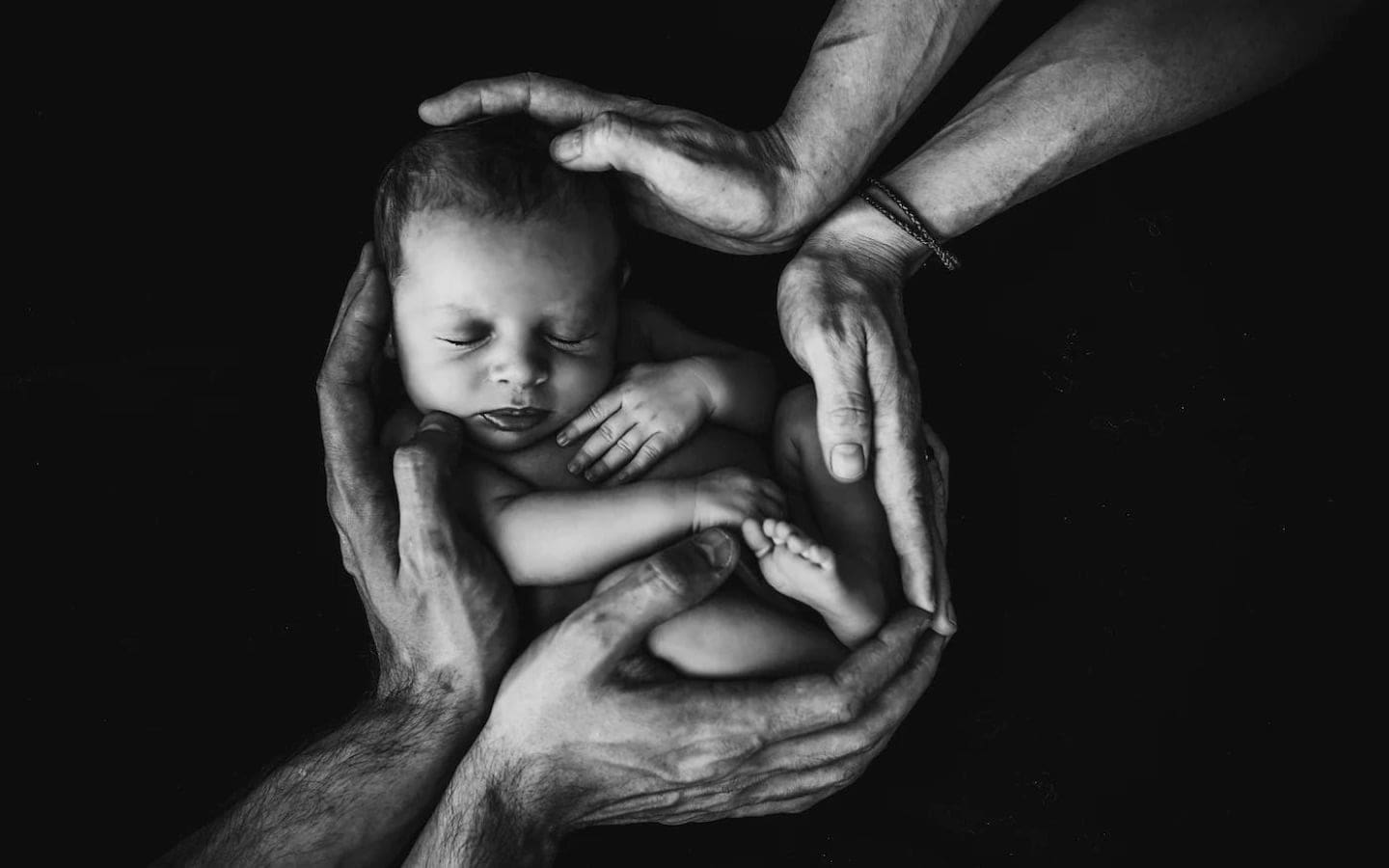 Parents cradling baby with both their hands.
