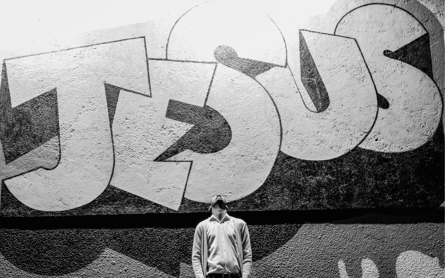 A photo of a man standing under a mural that reads “Jesus”