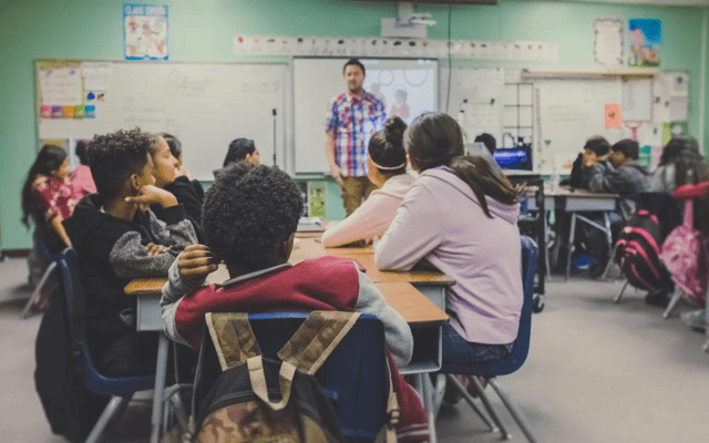 A classroom with a teacher standing in front talking to students.