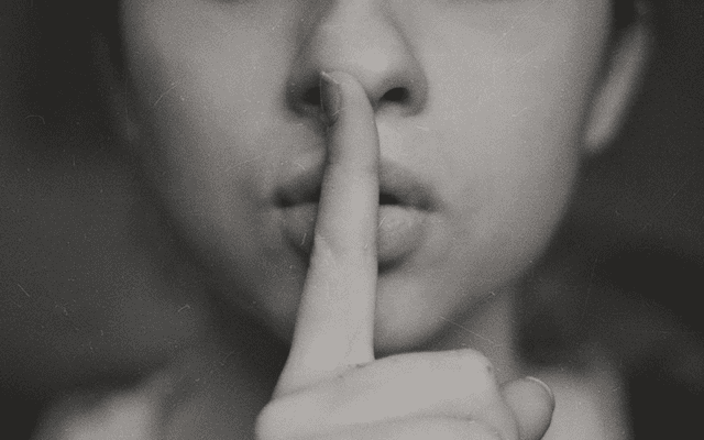 A woman in grayscale with her index finger over her lip.