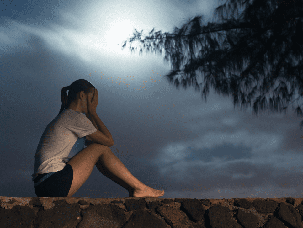 A girl showing signs of loneliness sitting on a rock fence.