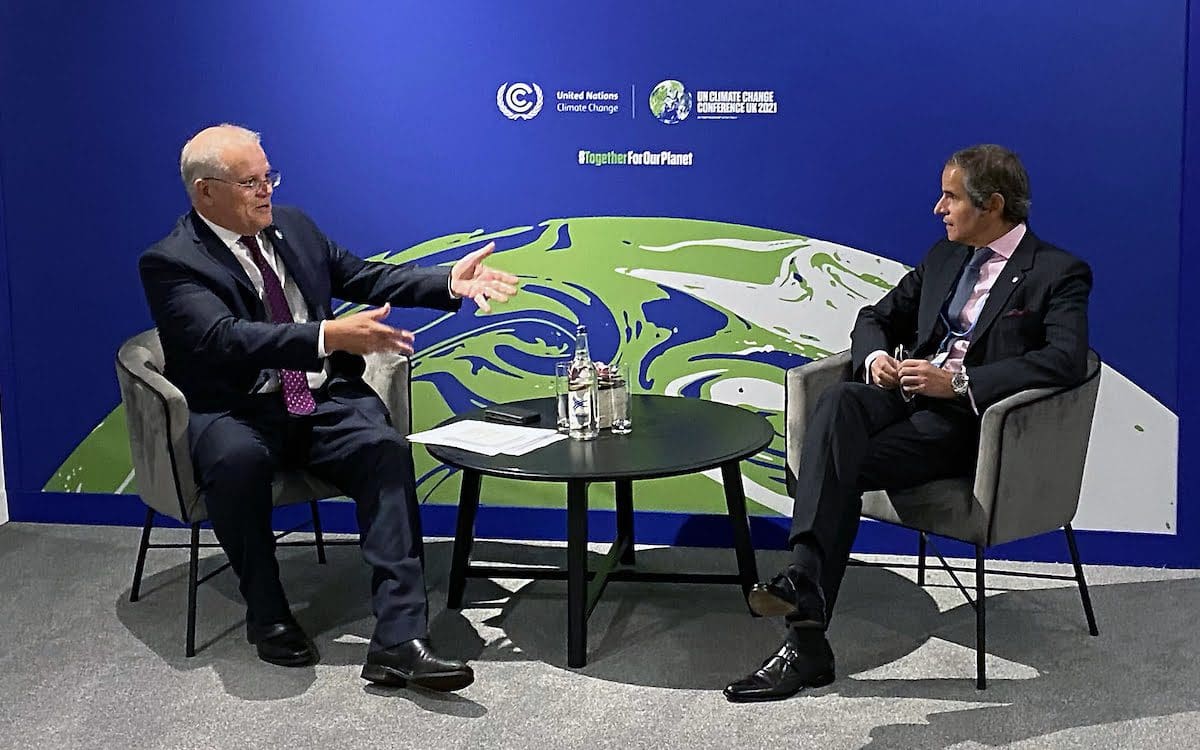 Two men sitting in chairs with a small table between them talking.