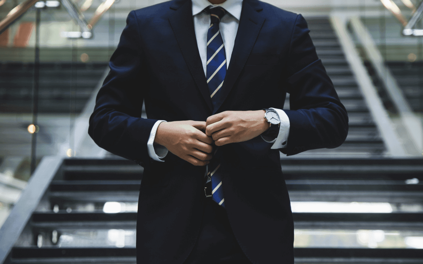 The torso of a man in a suit standing on steps in a business building.
