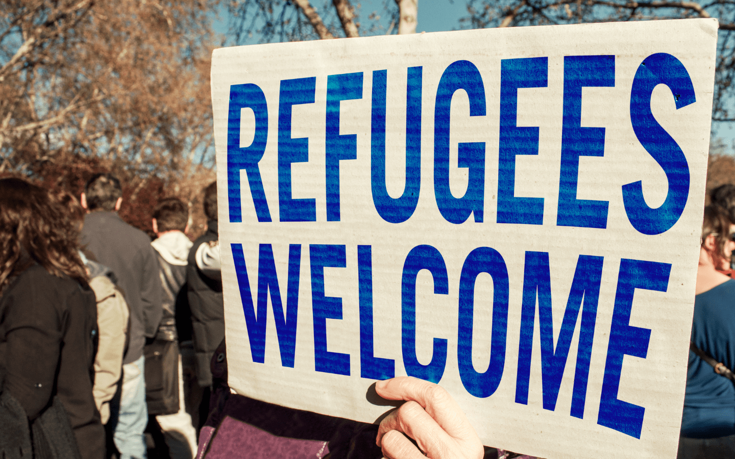A photo of a person holding a sign reading “Refugees Welcome.”