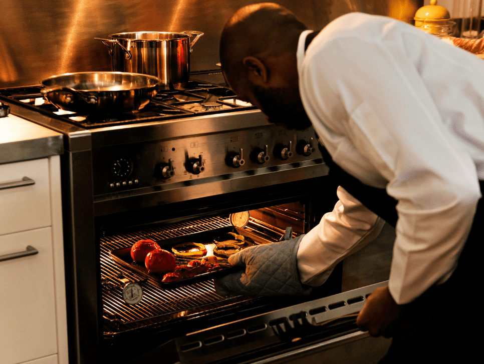 A cook checking on vegetables roasting in an oven.