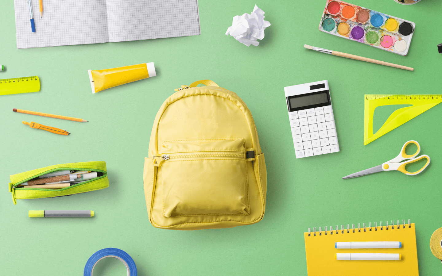 A photo of school supplies spread out onto a green surface.