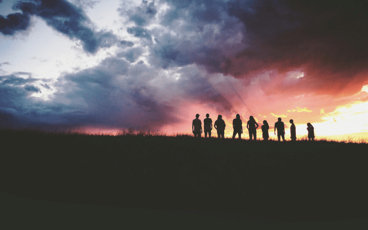 A photo of several people on a hill at sunset standing together.