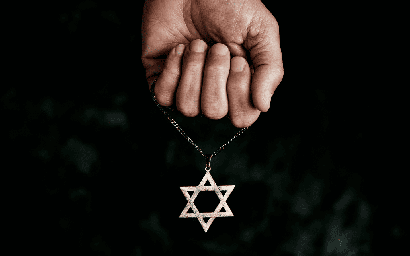 A photo of a hand holding a necklace of a Star of David.