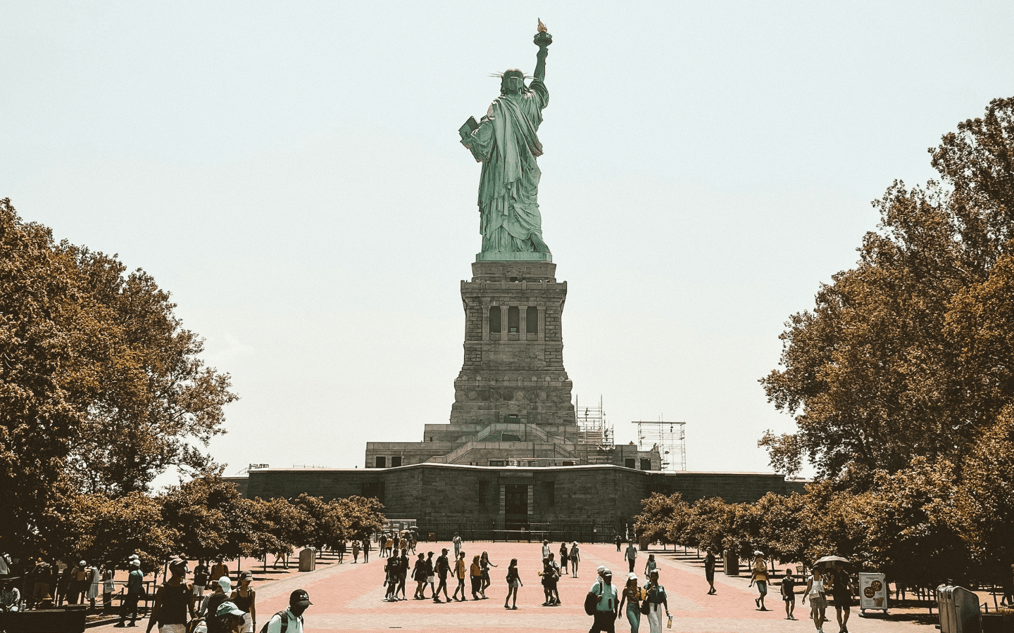 A photo of visitors walking along the base of the Statue of Liberty on Ellis Island.