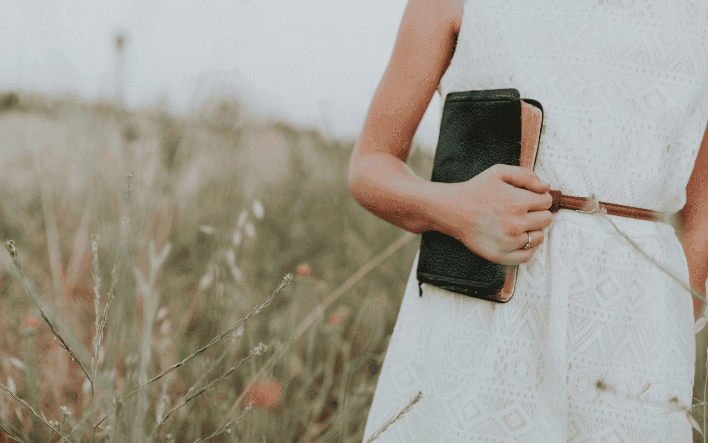 A woman holding a bible in a field.