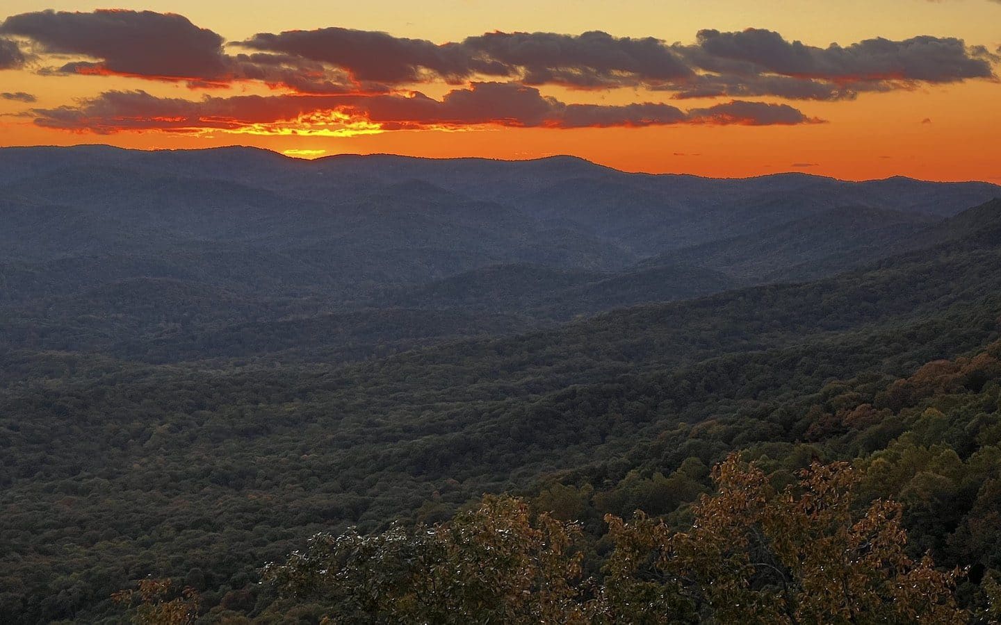 The sun setting over a valley in north Georgia.|Water flowing over rocks with fall-colored leaves on trees in the background.
