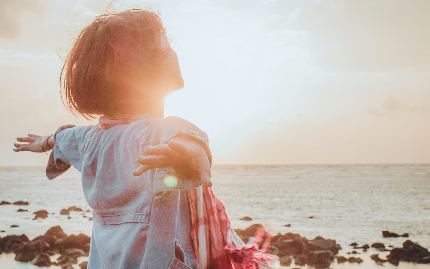 : A woman standing by the ocean with her arms outstretched watching the sunrise.