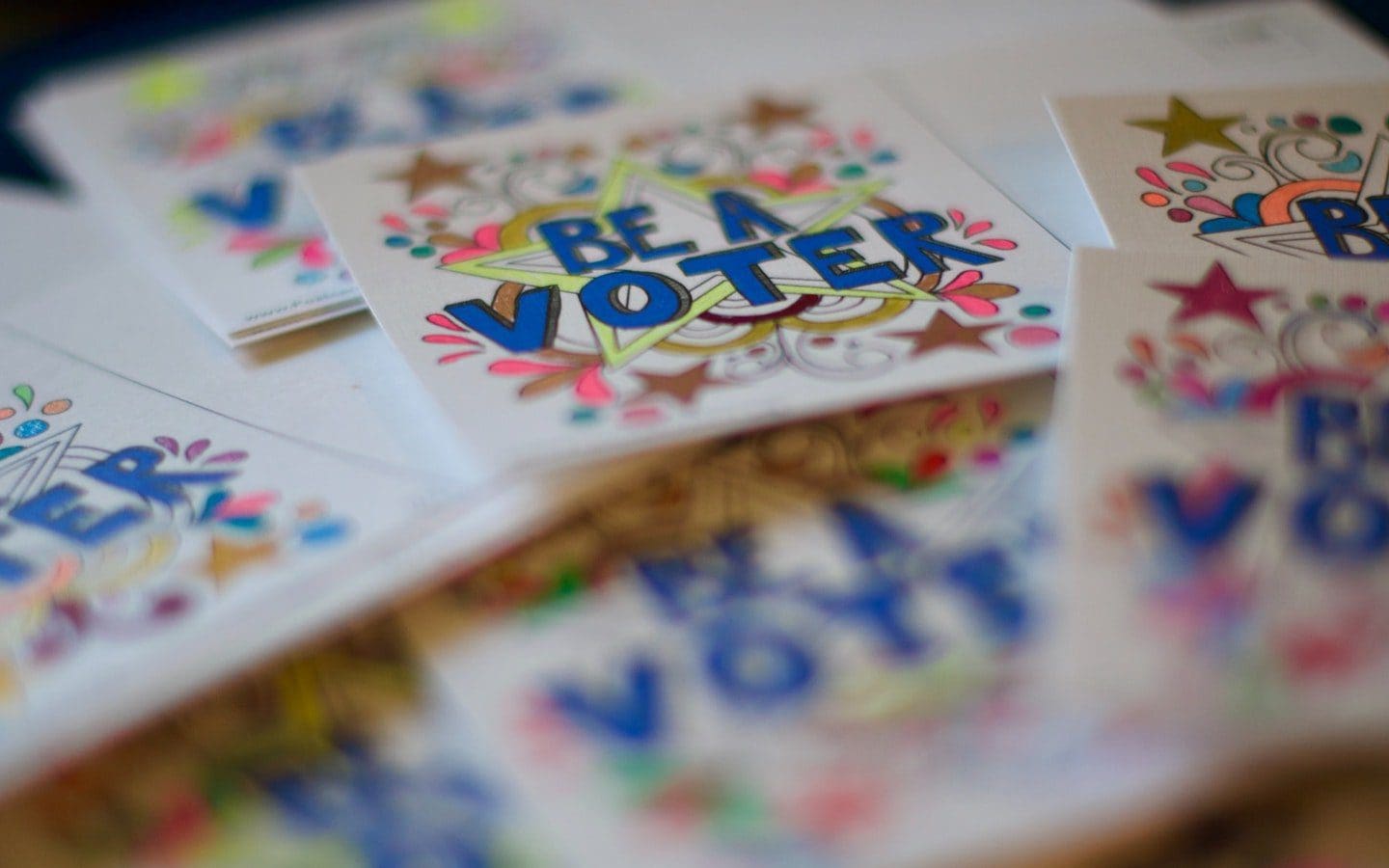 A stack of white cards with “Be a Voter” on them and a colorful illustration around the words.
