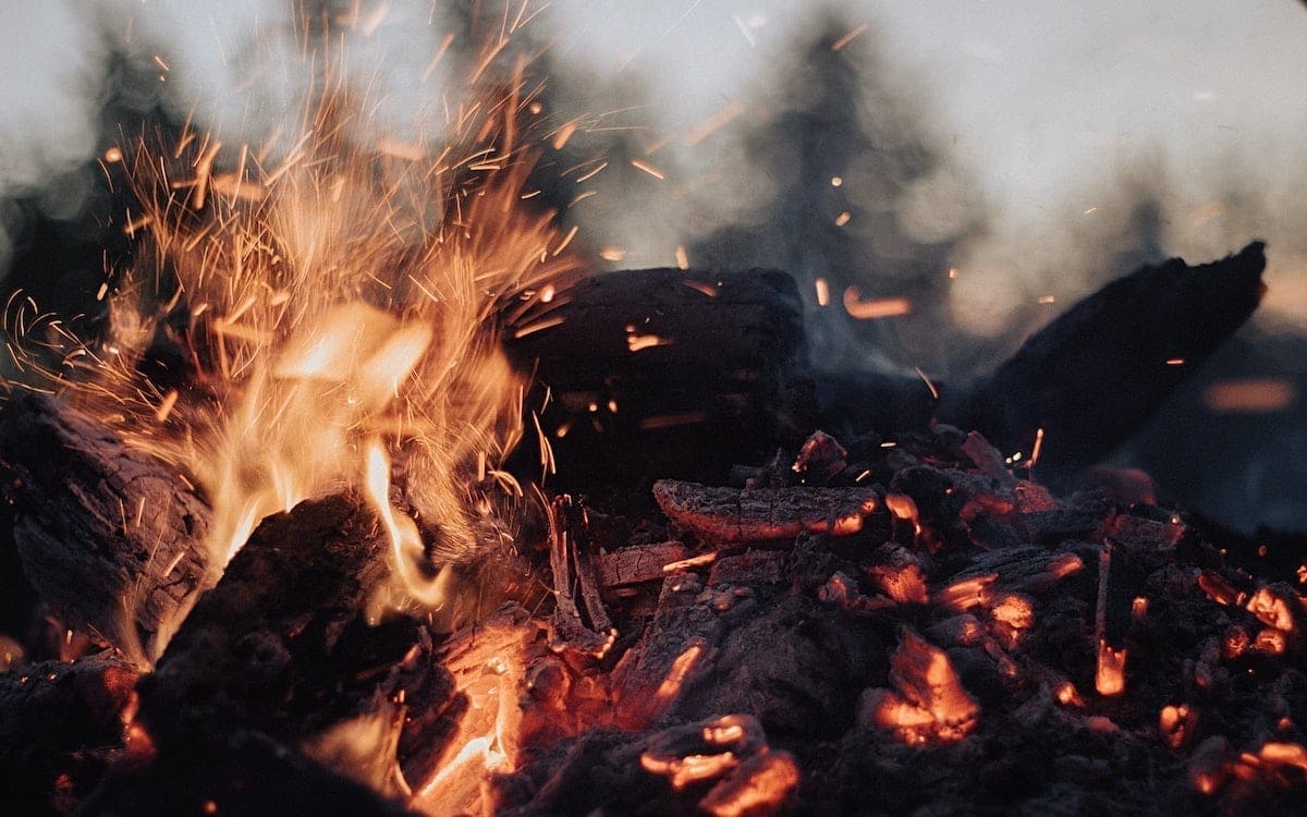 A campfire with sparks and flames on the left and lower flames and wood pieces on the right.