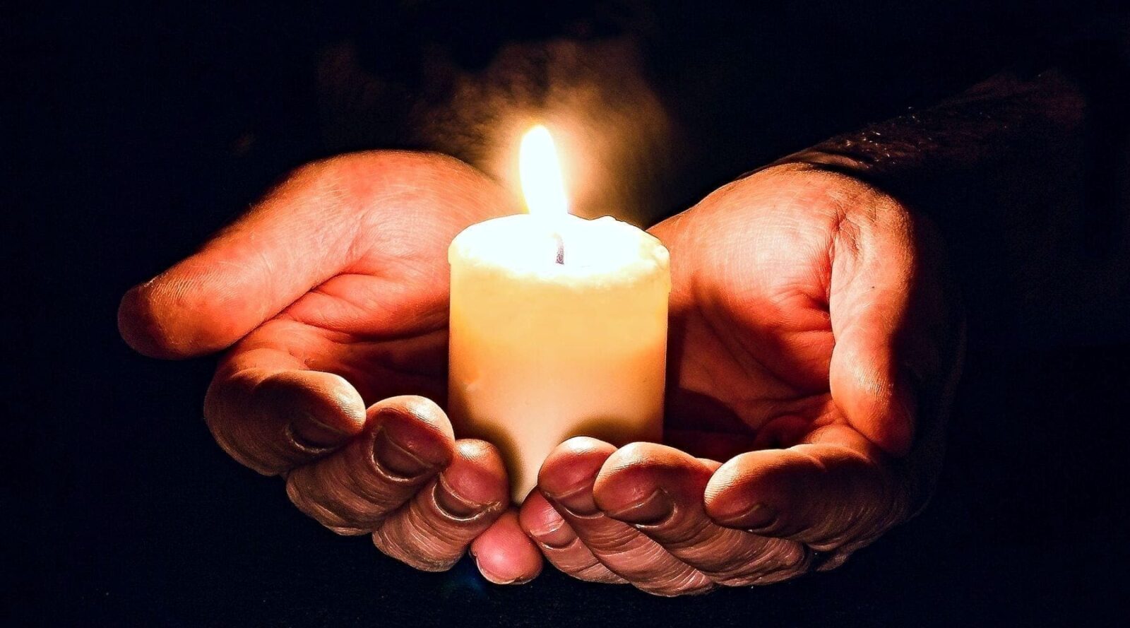 Two hands cradling a lit candle