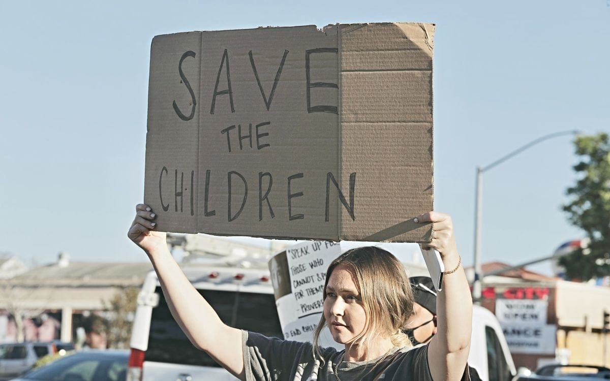 Young woman holding up cardboard sign reading Save The Children