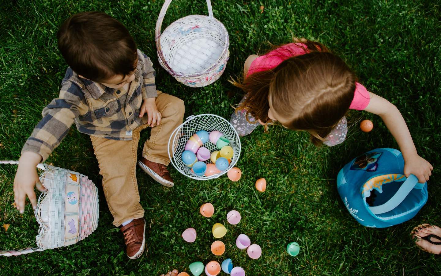 Two children sitting on the ground with easter eggs and baskets next to them seen from above.