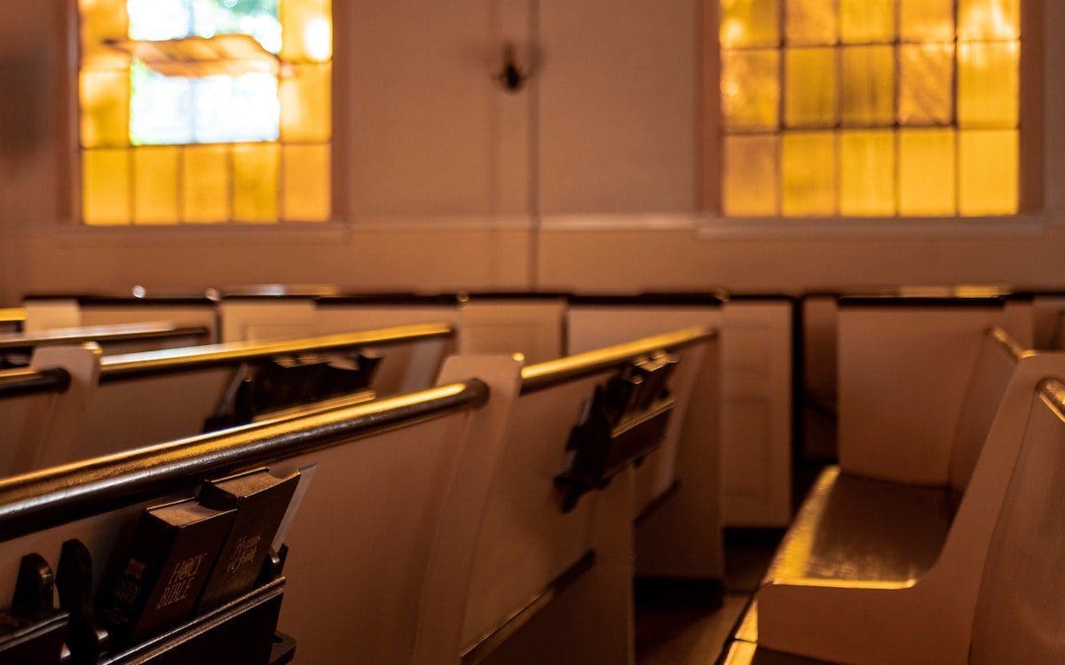 Church pews with sun shining through stained glass windows.