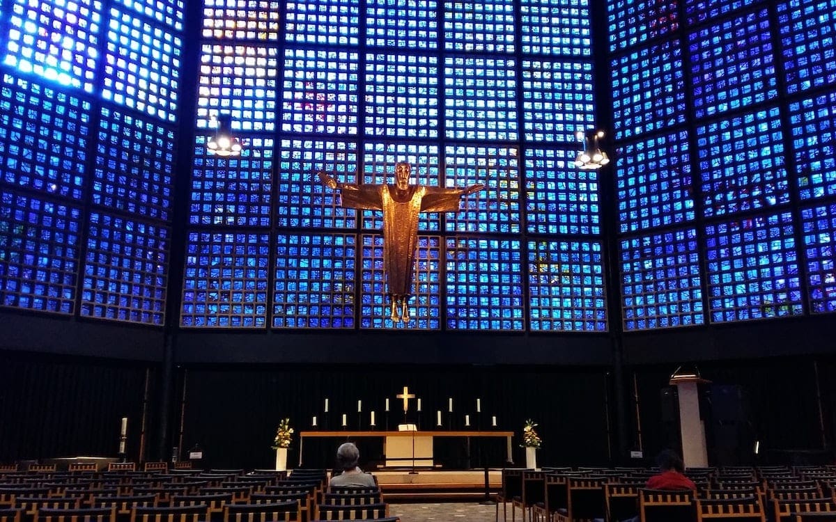 A church sanctuary with a Jesus icon suspended in the air and a few people sitting in the pews.