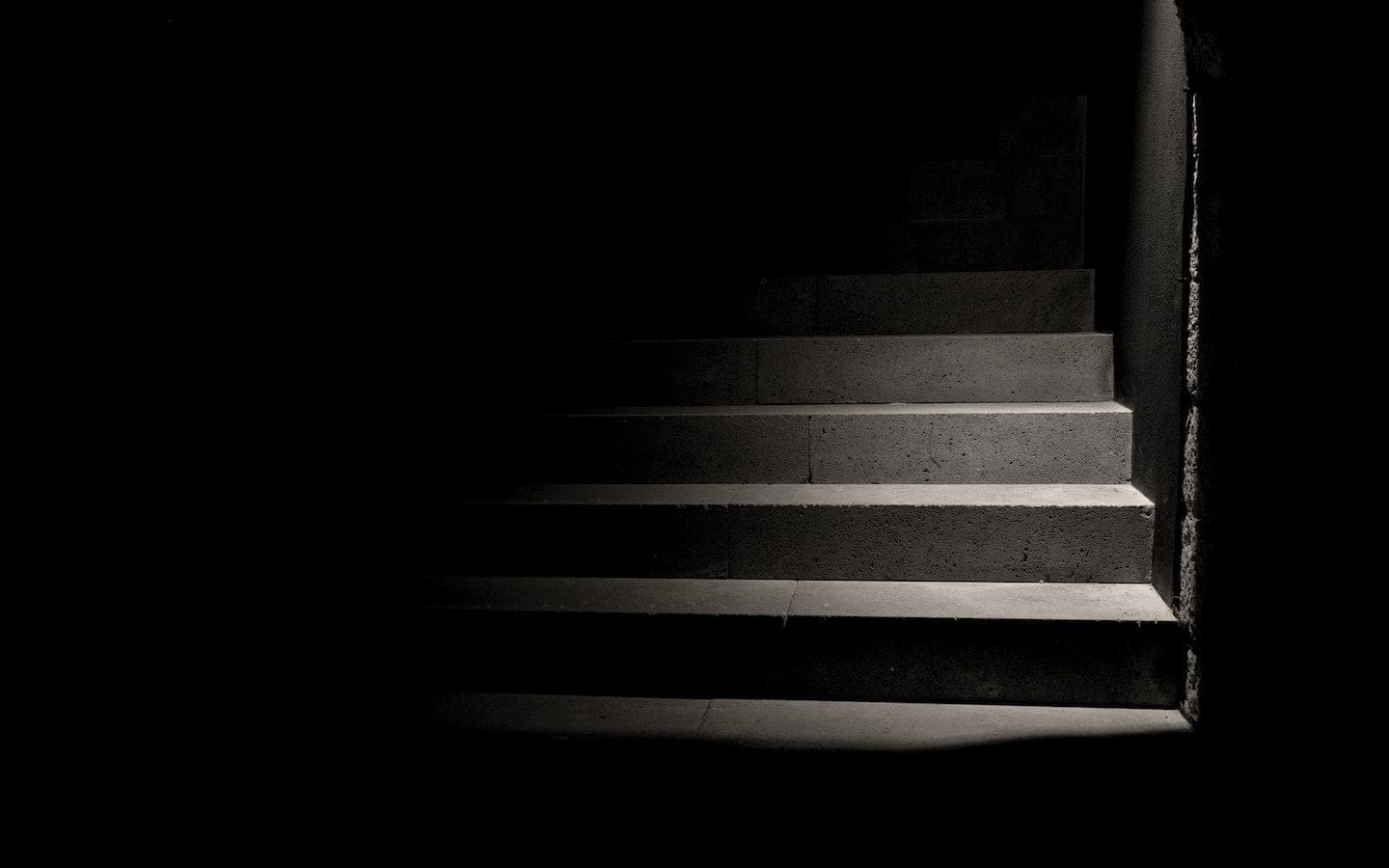A set of concrete stairs in a dark room with only a few steps illuminated.