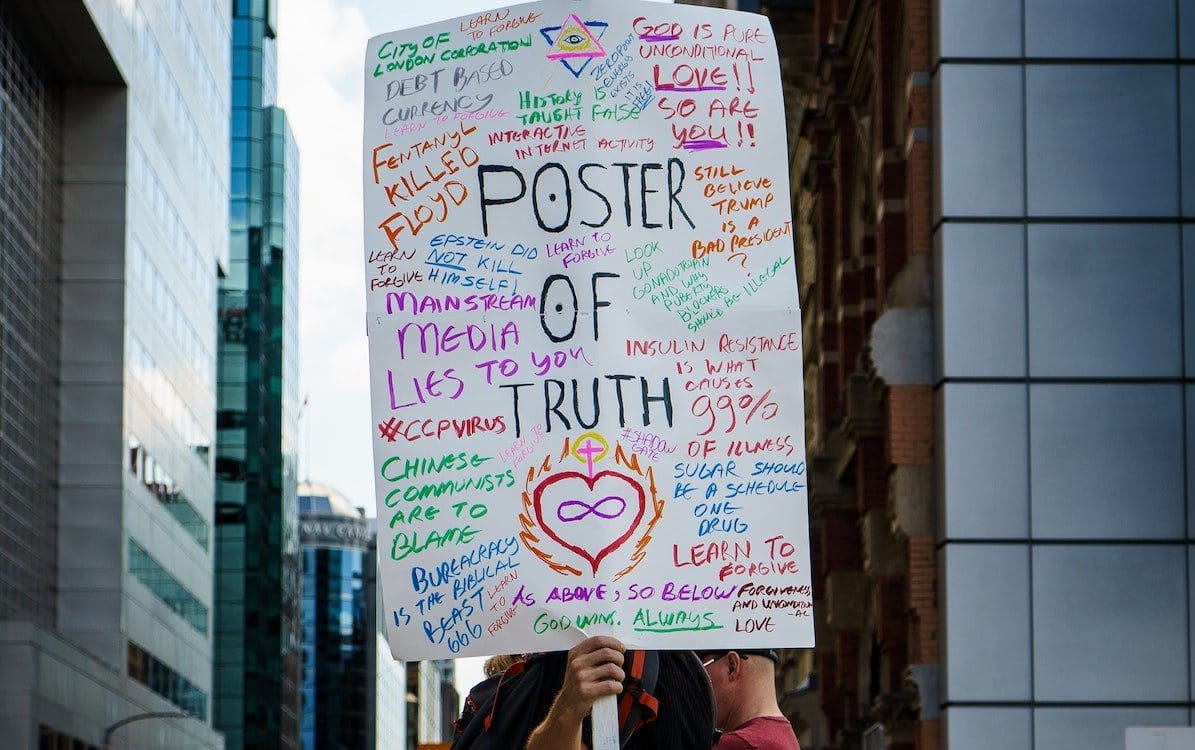 A man holding a sign filled with conspiracy theories that says “Poster of Truth” in the middle.
