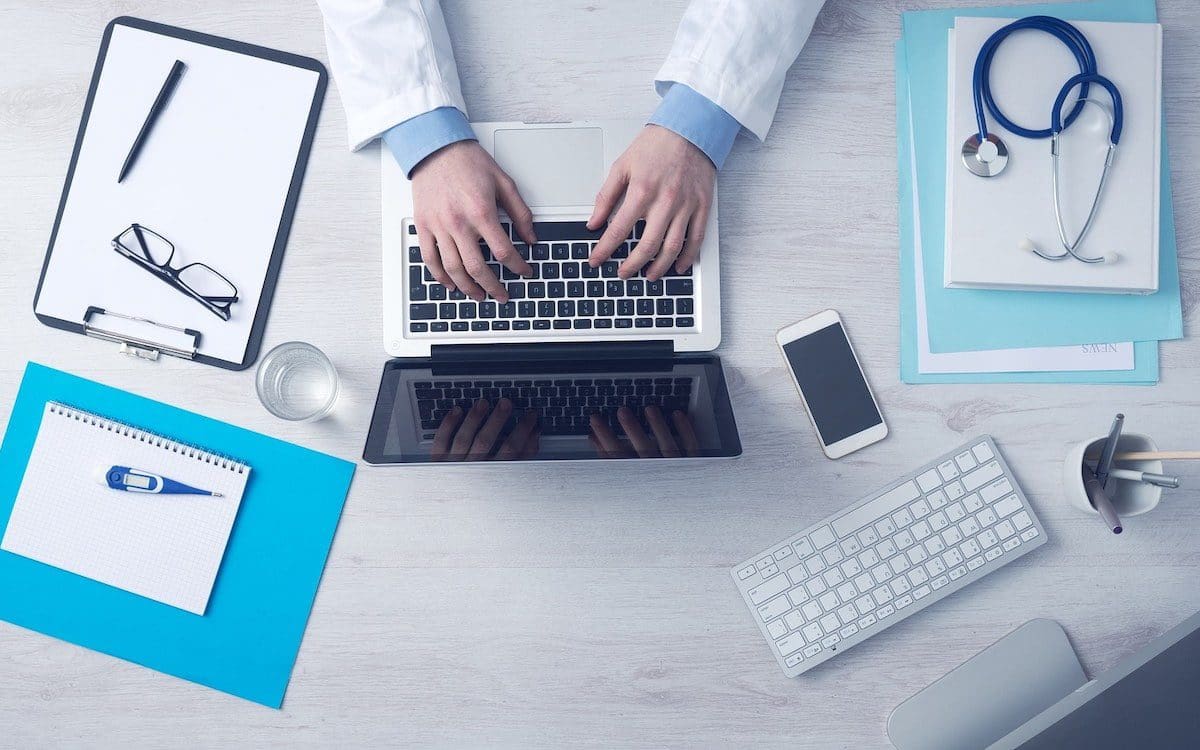 A doctor sitting at a desk seen from above with a computer