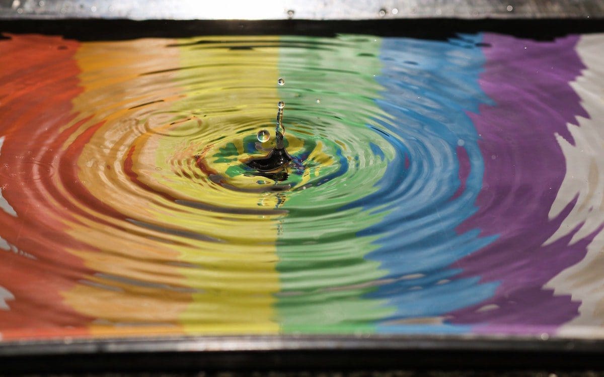 A rainbow reflected in water with ripples resulting from a splash in the middle.