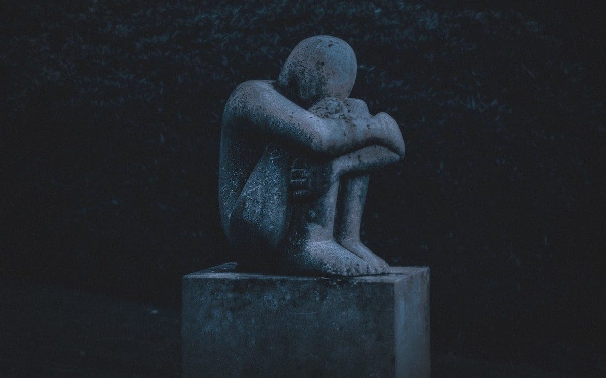 A stone statue of a person sitting and hugging their knees.