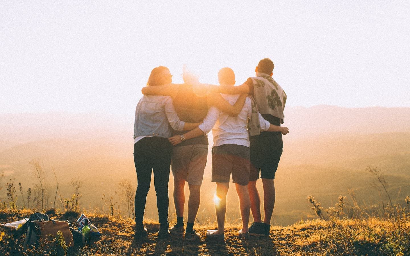 A group of four people with arms around each other watching the sunrise at a scenic overlook.