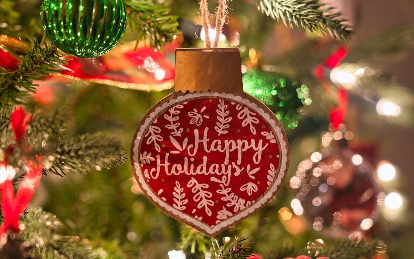 A red ornament on a pine tree that says