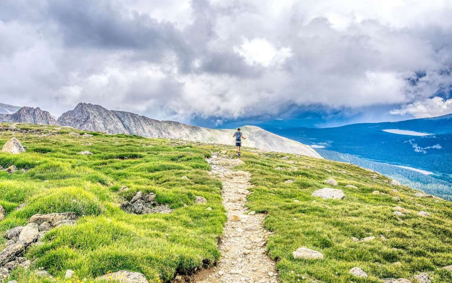 A hiking trail in the mountains with a single person hiking on it.