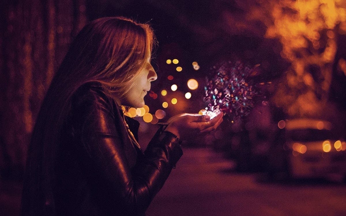 A woman blowing out breath and colors emerging from her hands.