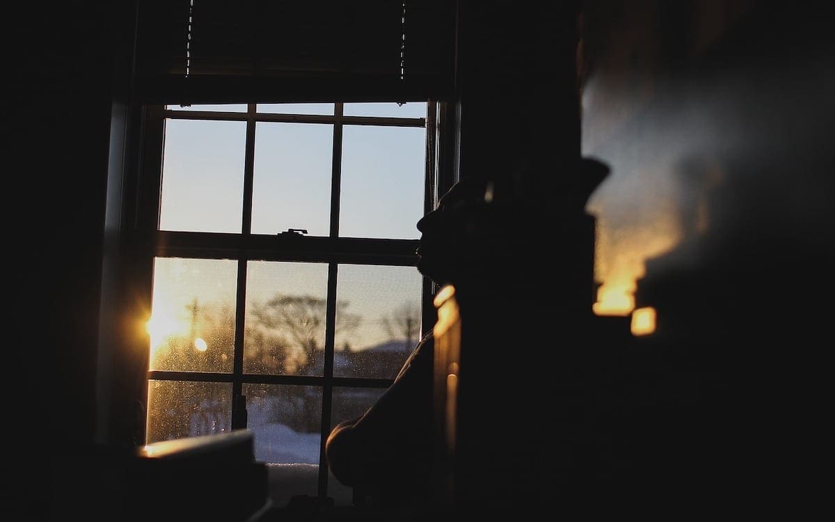 A man sitting on a bench in a darkened room with a hint of sunlight coming in through the window.