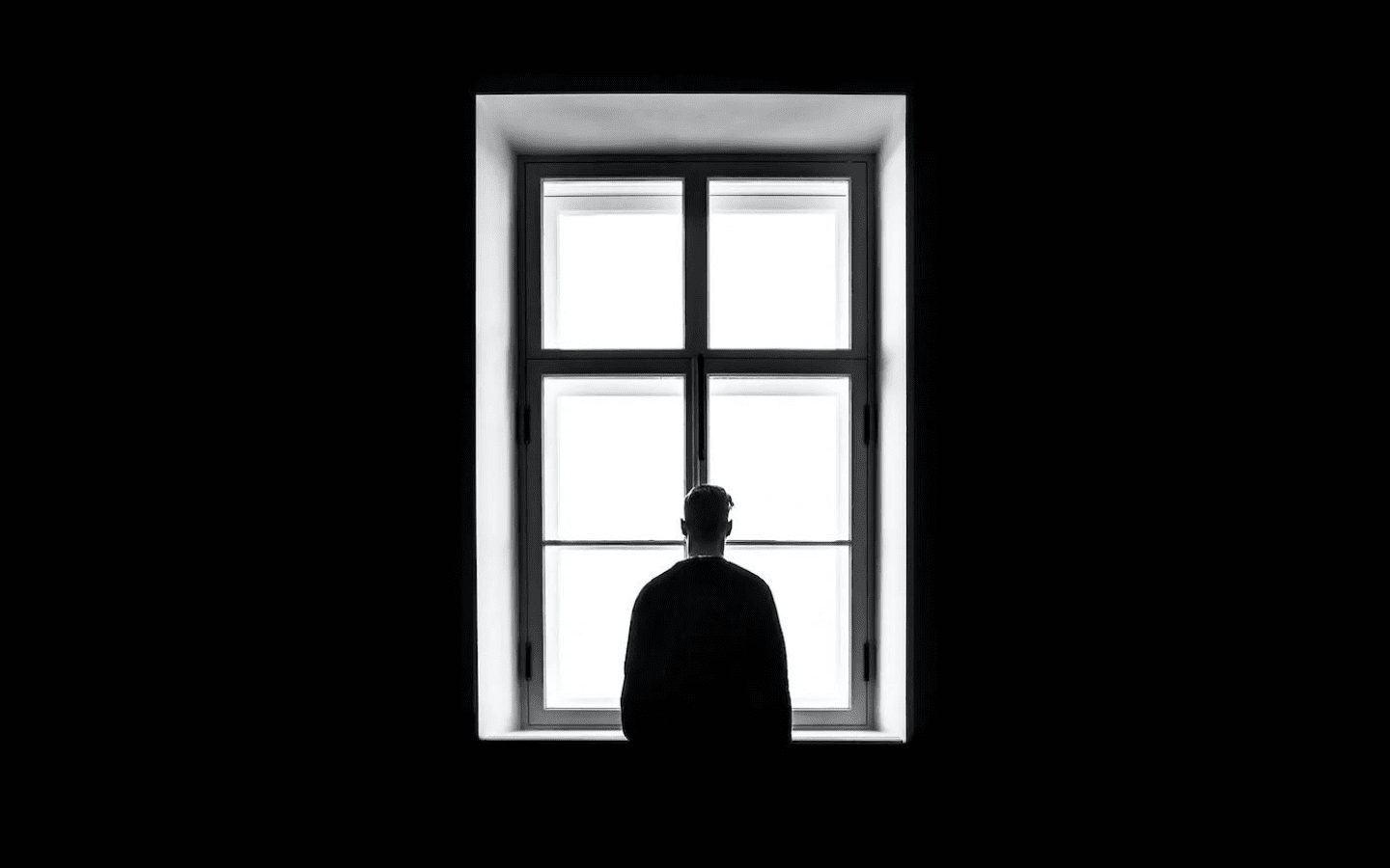 Black and white image of man looking out of a window.