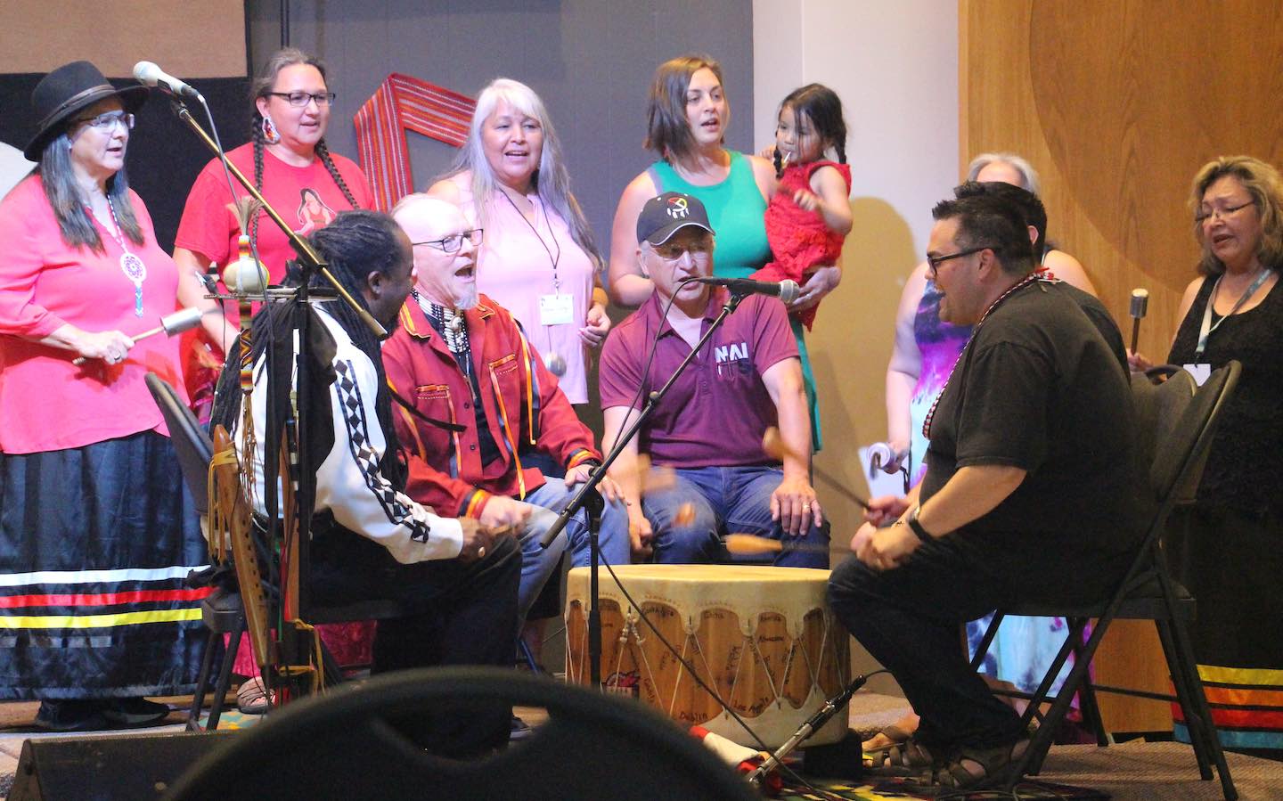 A group of people sitting in a circle with a drum in the middle.