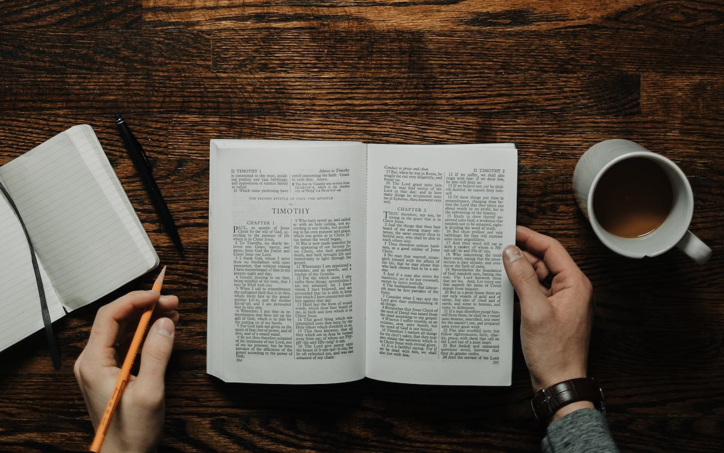 A person seen from above sitting at a desk with an open Bible in front of them.