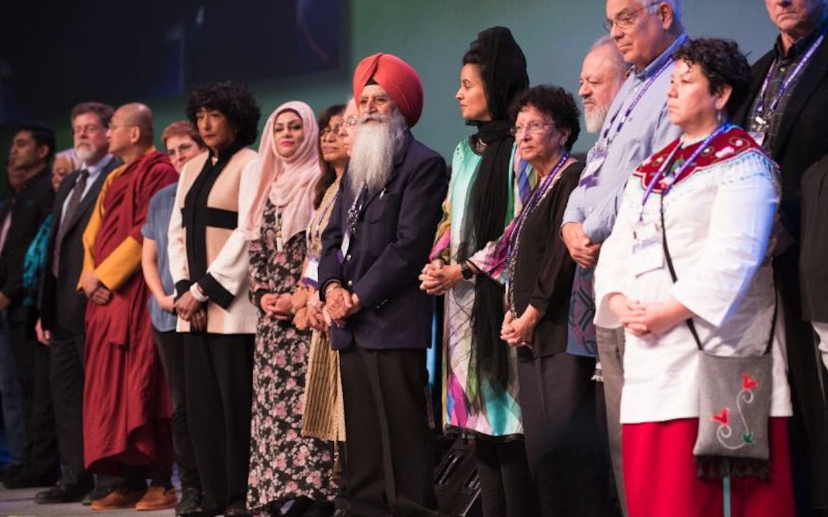 A row of people from several faith traditions standing together on a stage.|Logo for the Parliament of the Worlds' Religions 2021 virtual gathering.