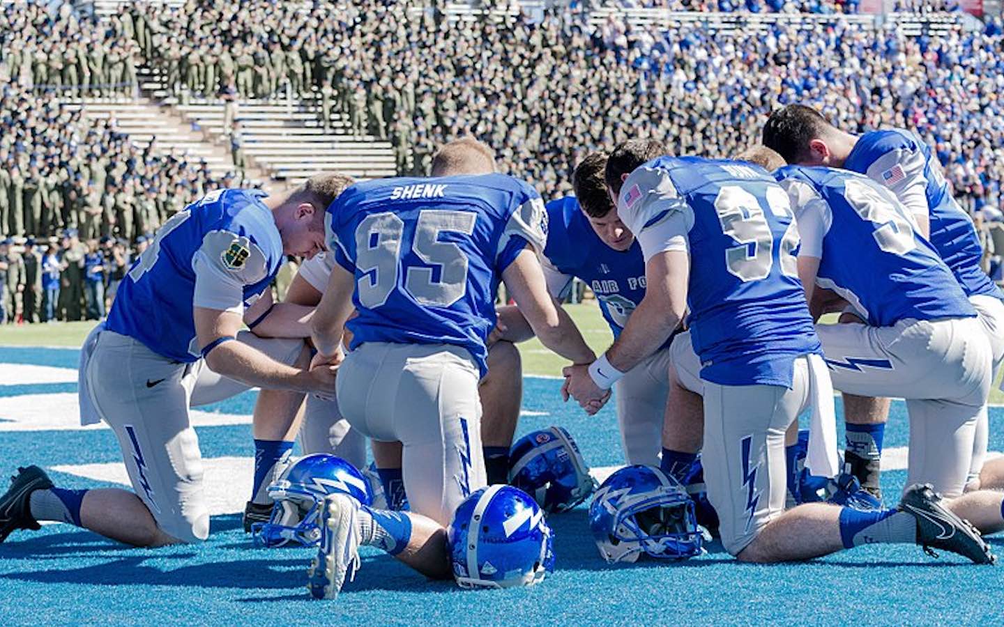 Football players kneel in the endzone to pray together before a football game.