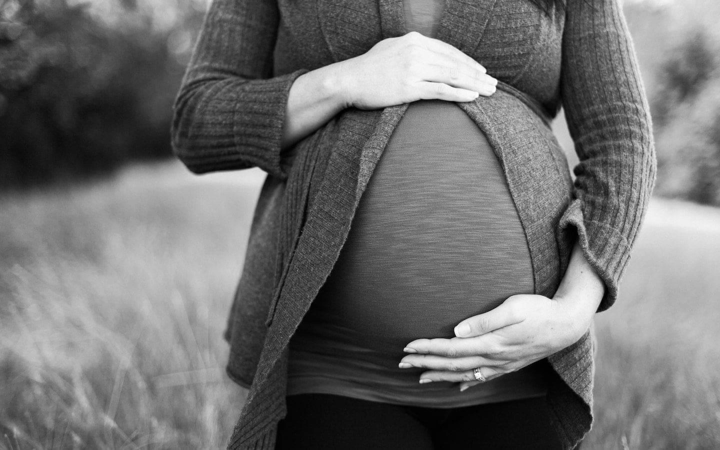 A grayscale image of a pregnant woman standing in a field with her hands on her stomach.