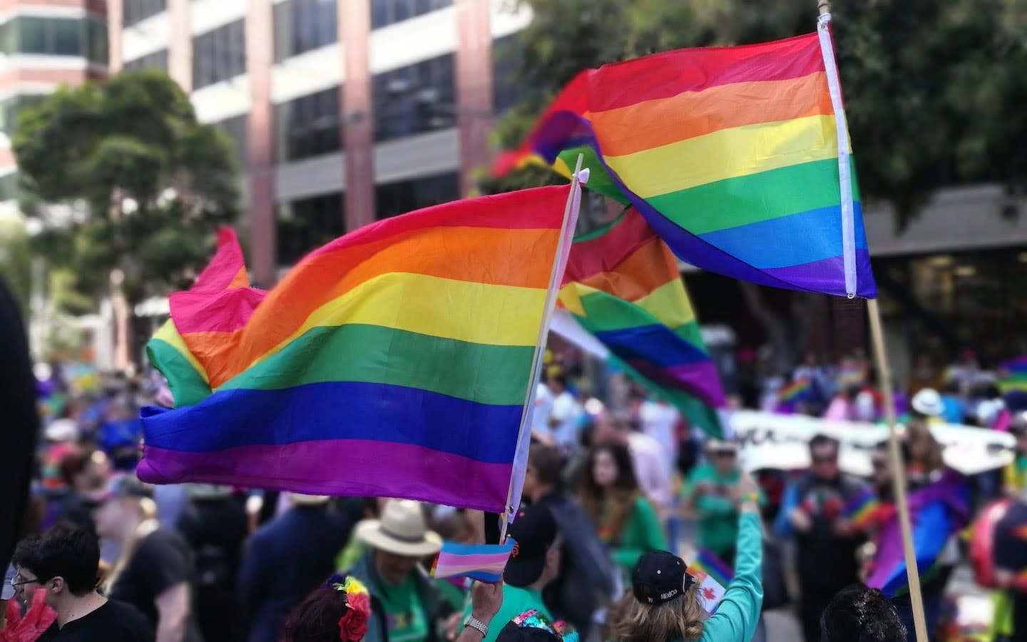 A group of people outside in a parade with two people holding pride flags.